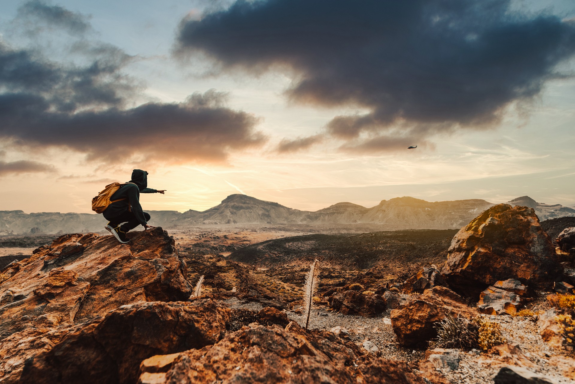 Success hiker hiking on sunrise mountain peak pointing to the sky.